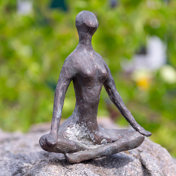 Kleine Figur sitzt im Yogasitz auf einem Stein in der Natur